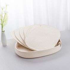 a white vase sitting next to three woven placemats on a table with flowers in the background