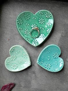 three heart shaped dishes sitting next to each other on top of a cement slab with a ring in the middle