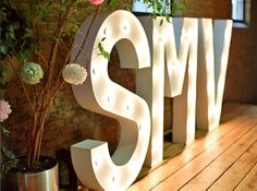 the word smile is lit up in front of flowers and potted plants on a wooden floor