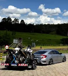 two motorcycles are on the back of a car in front of a fenced area