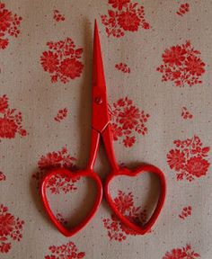 a pair of red scissors sitting on top of a flowered tablecloth covered with flowers