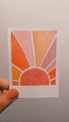 a hand holding up a piece of paper with an orange and pink design on it