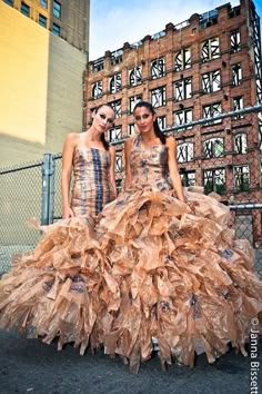 two women standing next to each other wearing dresses made out of paper mache sheets