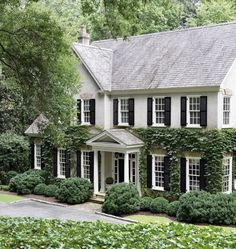 a large white house with black shutters and ivy growing on the side of it