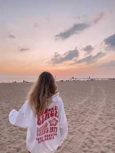 a woman standing on top of a sandy beach next to the ocean in front of a sunset