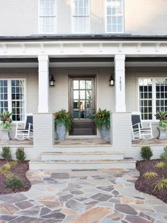 the front entrance of a house with two white chairs and flowers on each side of the door