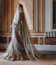 a woman in a wedding dress with a veil on her head standing next to a wall