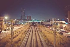 an empty train track at night with the city lights in the background