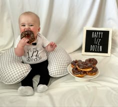 a baby sitting on a bed with donuts in front of him and a sign that says happy 17th birthday