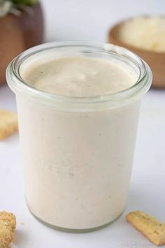 a glass jar filled with white liquid next to crackers on a table and in the background is a potted plant