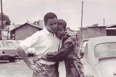 a black and white photo of a man hugging a woman in front of a car