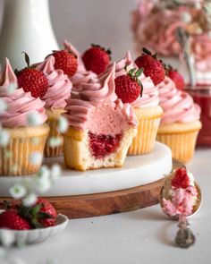 some cupcakes with pink frosting and strawberries on top are sitting on a plate