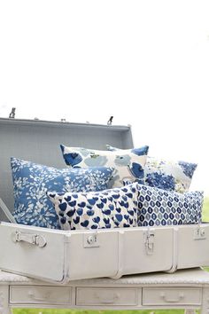 a trunk filled with lots of pillows on top of a bed covered in blue and white