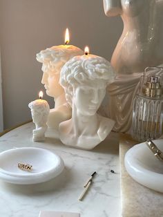 a marble table topped with candles next to a white busturine and other items