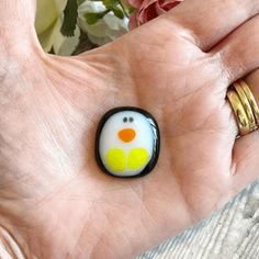 a person's hand holding a ring with a yellow and white penguin on it