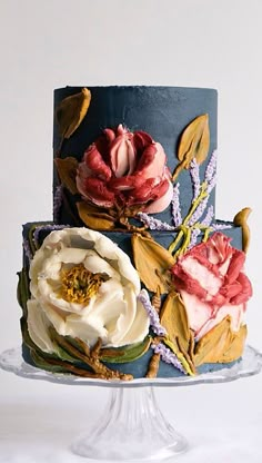 a three tiered cake decorated with flowers and leaves on a glass stand against a white background