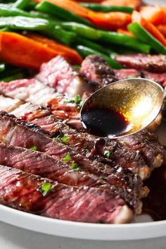 a plate with steak, carrots and asparagus on it next to a spoon