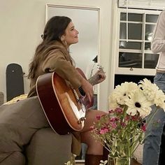 a woman sitting on a couch with a guitar in front of her and another man standing behind her