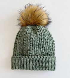 a green knitted hat with a brown fur pom - pom on top