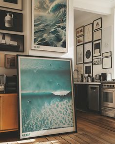 there are pictures on the wall above the kitchen counter and in front of it is a surf poster