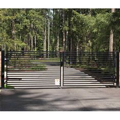 an iron gate with wooden posts in front of a driveway and trees on the other side