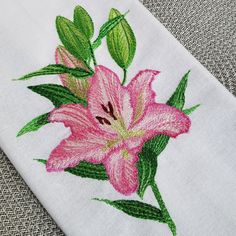 a pink flower is embroidered onto a white cloth with green leaves on the edges and bottom