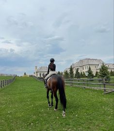 a woman riding on the back of a brown horse across a lush green field with homes in the background