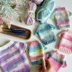 crocheted baby sweaters and mittens laid out on a table with yarn