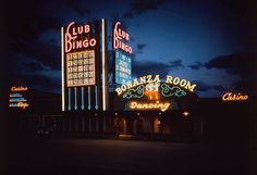 several neon signs are lit up on the side of a building at night, with dark clouds in the background