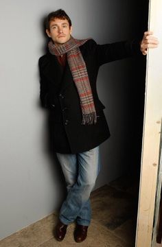 a man standing in front of a door wearing a coat and scarf with his arms out