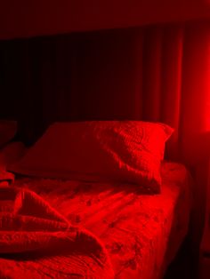 a red light shining on a bed in a dark room with pillows and blankets folded over it