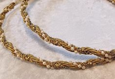 two gold necklaces with pearls and beads on a white tablecloth, one in the shape of a snake