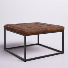 a brown leather ottoman sitting on top of a metal frame table with an open end