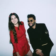 a man and woman posing for a photo in front of a white wall wearing sunglasses