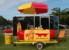 a yellow and red hot dog cart sitting on top of a lush green field