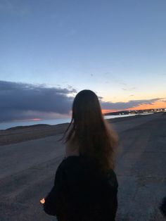 a woman standing on the side of an empty road at dusk with her back to the camera