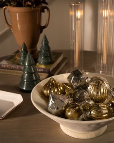 a white bowl filled with gold and silver foiled christmas ornaments on top of a wooden table