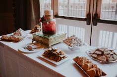 a table topped with lots of desserts and pastries next to a window filled with windows