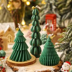 three green christmas trees are sitting on a wood slice in front of some other holiday decorations