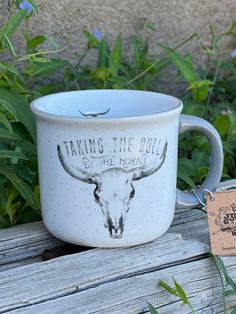 a ceramic mug with the words taking the bull by the horns is sitting on a wooden bench