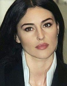 a woman with long black hair wearing a suit and white shirt is looking at the camera