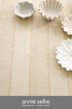 three white dishes sitting on top of a beige cloth covered table with the words annie selke written below it