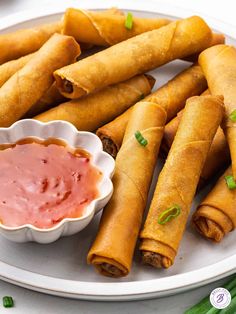 several spring rolls on a plate with dipping sauce in a small bowl next to them