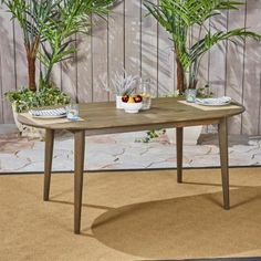 a wooden table with plates and bowls of fruit on it in front of two potted plants