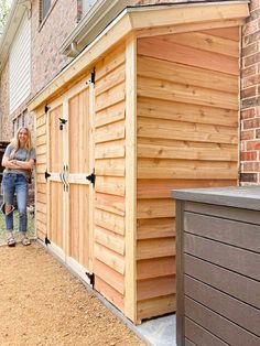 a woman standing next to a wooden shed on the side of a building with its door open