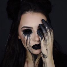 a woman with black makeup holding her hands to her face