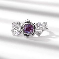 a ring with a purple stone in the center and white diamonds around it on a white background