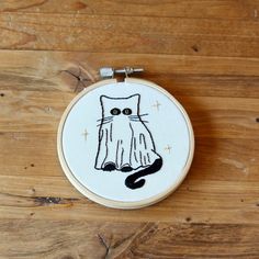 a hand embroidery kit with a black and white cat on it's face, sitting on a wooden surface