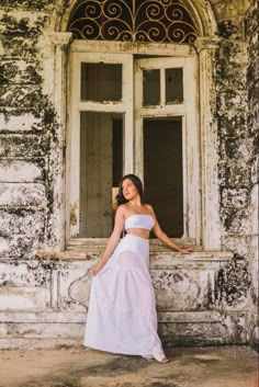 a woman standing in front of a window wearing a white dress and holding her arms out