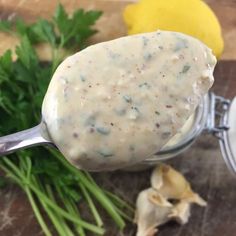 a spoon full of mayonnaise sitting on top of a cutting board next to garlic and parsley